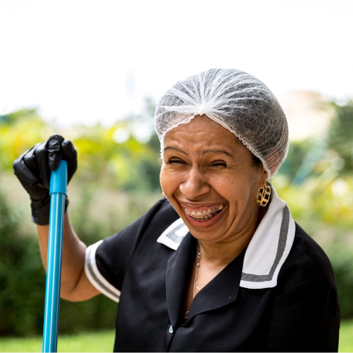 Smiling cleaning professional wearing a uniform and gloves, holding a cleaning tool, in a lush outdoor setting, representing Route 9 Cleaning Services' commitment to quality residential and commercial cleaning.